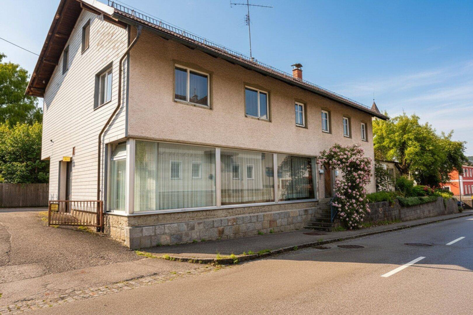 Vorderansicht des Wohnhauses mit großen Fenstern im Erdgeschoss und Rosenbusch.
