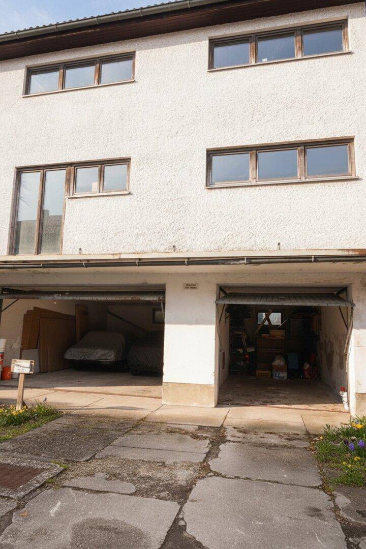 Vorderansicht des Gebäudes mit zwei Garagen und Fenstern im Obergeschoss.