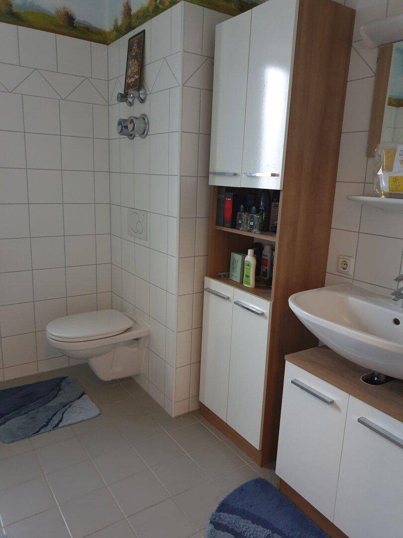 Helles Badezimmer mit weißen Fliesen, wandhängendem WC und modernem Waschbecken mit Unterschrank.