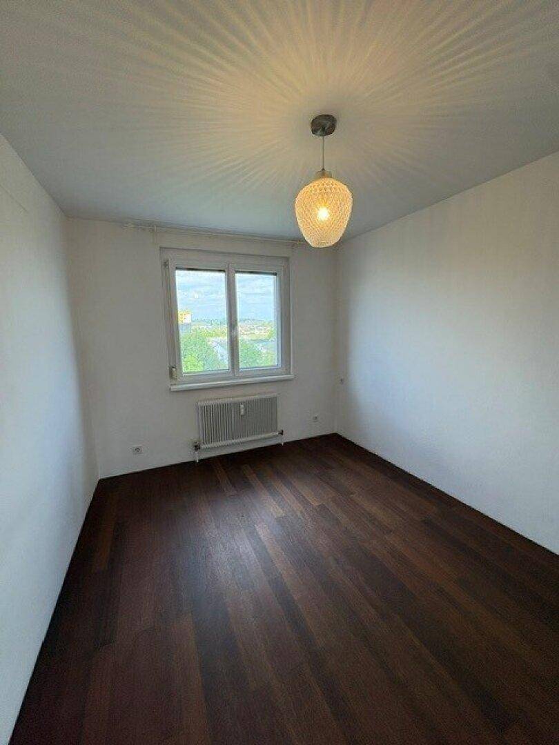 Helles Schlafzimmer mit dunklem Holzboden, Fenster und Blick ins Grüne.
