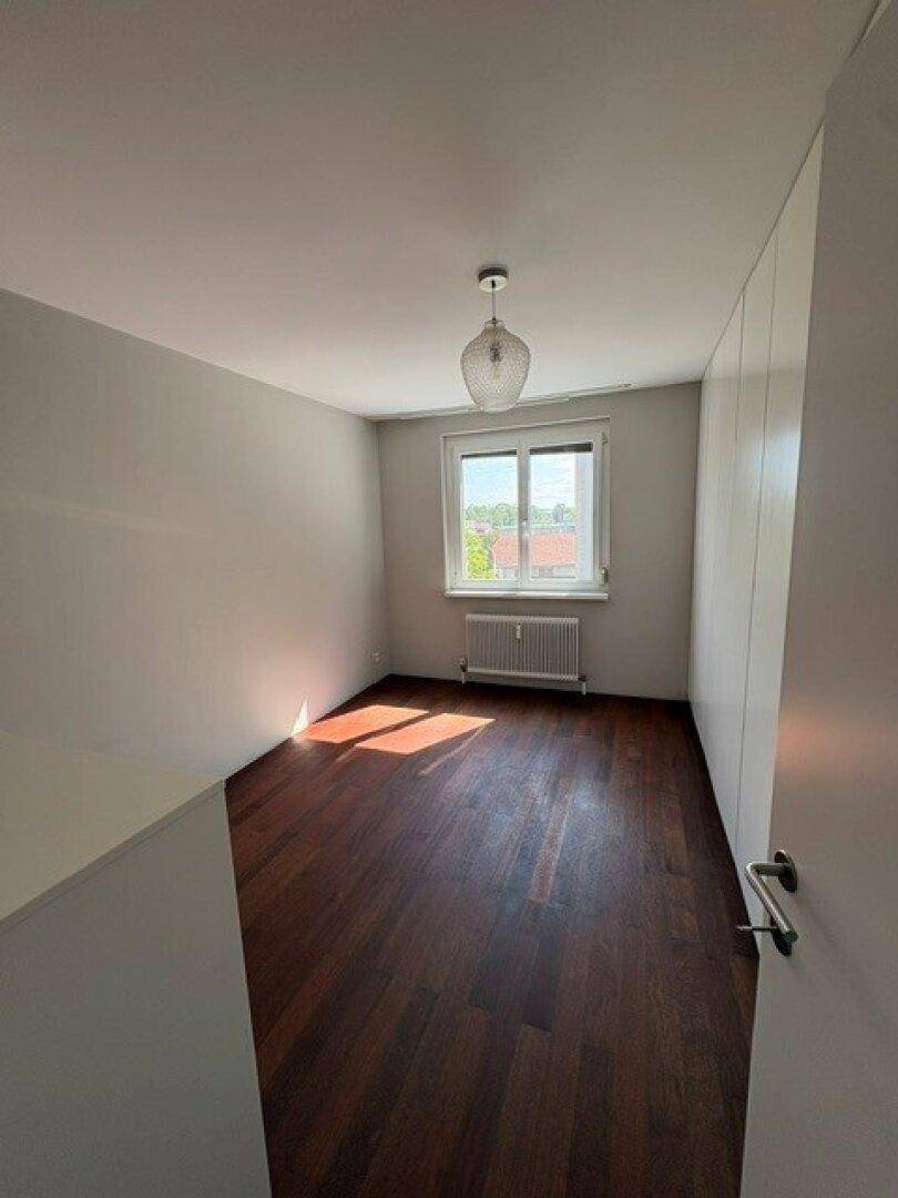 Helles Schlafzimmer mit dunklem Holzboden, Fenster und Einbauschrank.