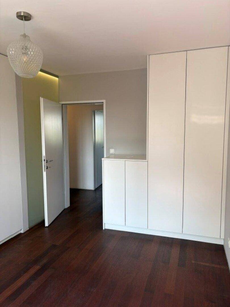 Schlafzimmer mit Einbauschränken, dunklem Holzboden und hellem Licht.