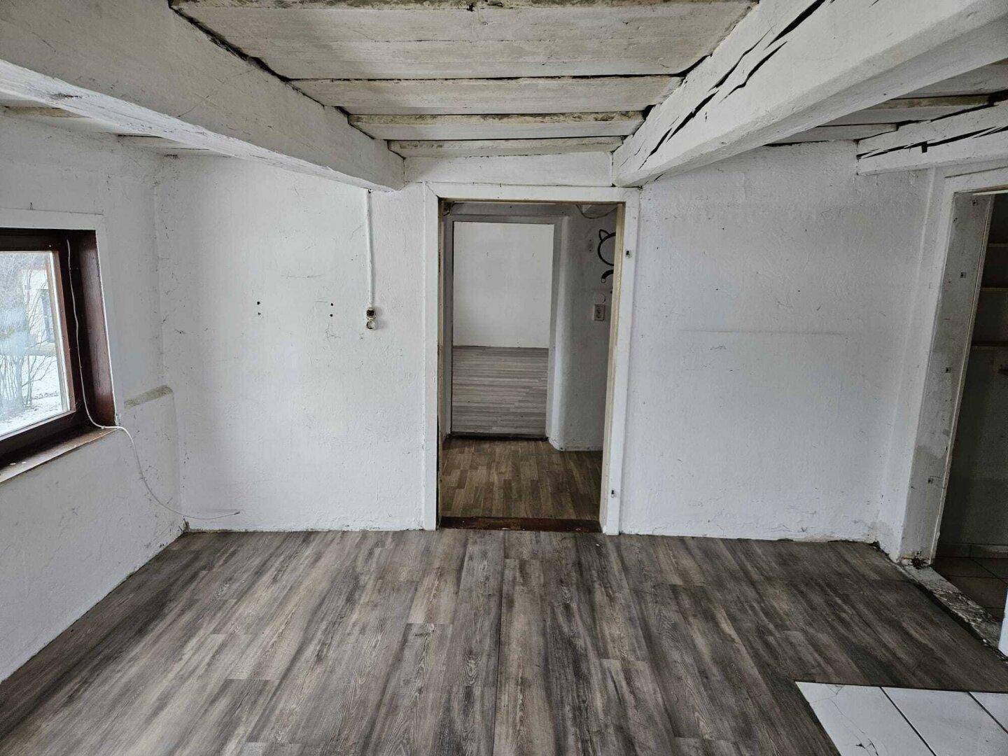 Renovierter Innenraum mit sichtbaren Holzbalken an der Decke und neuem Laminatboden.
