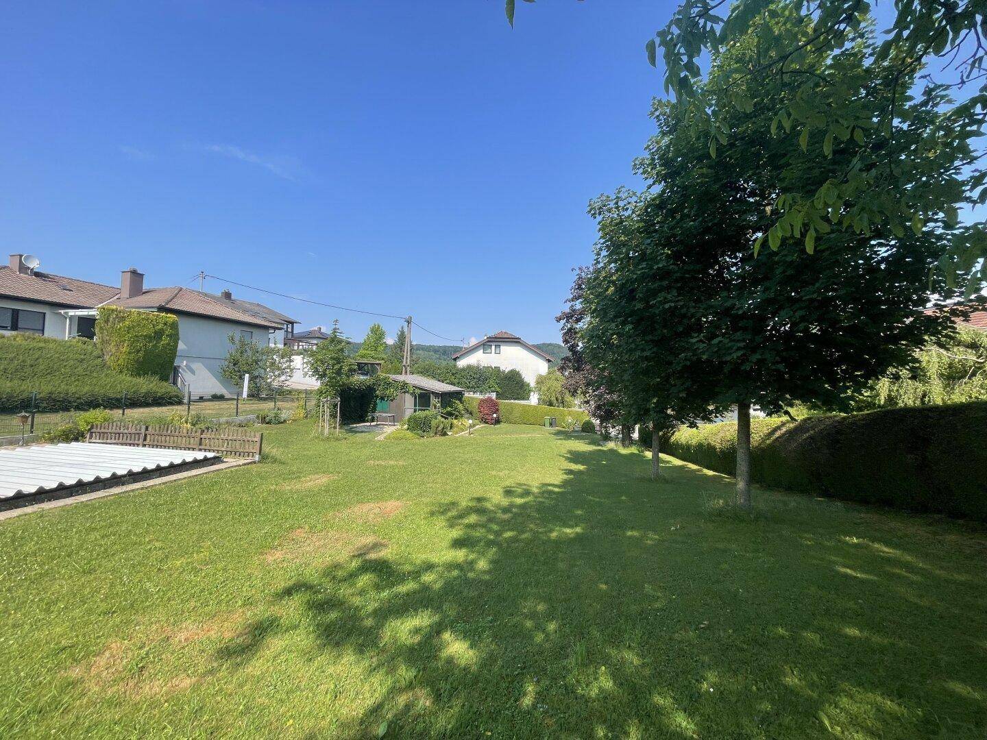 Weitläufiger Garten mit großer Rasenfläche, Bäumen und einem abgedeckten Pool im Hintergrund.