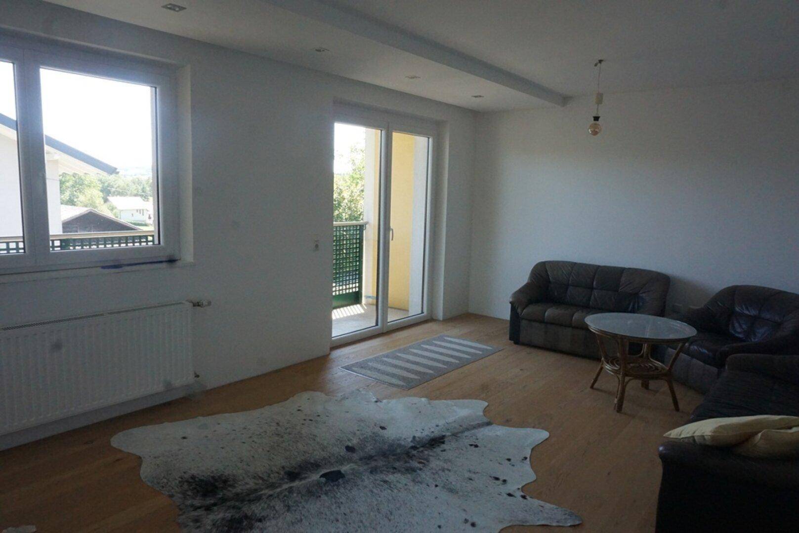 Geräumiges Wohnzimmer mit Parkettboden, Ledersofas und Zugang zu einem Balkon.