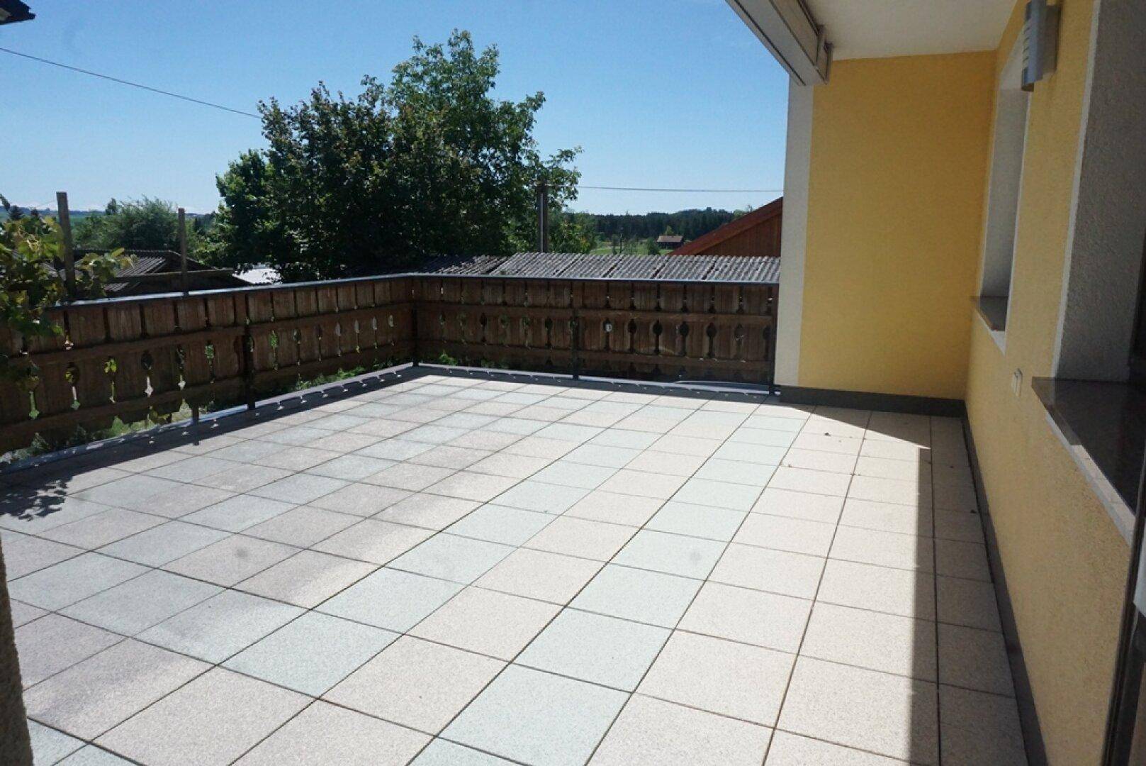 Große geflieste Terrasse mit Holzgeländer und sonnigem Ausblick ins Grüne.