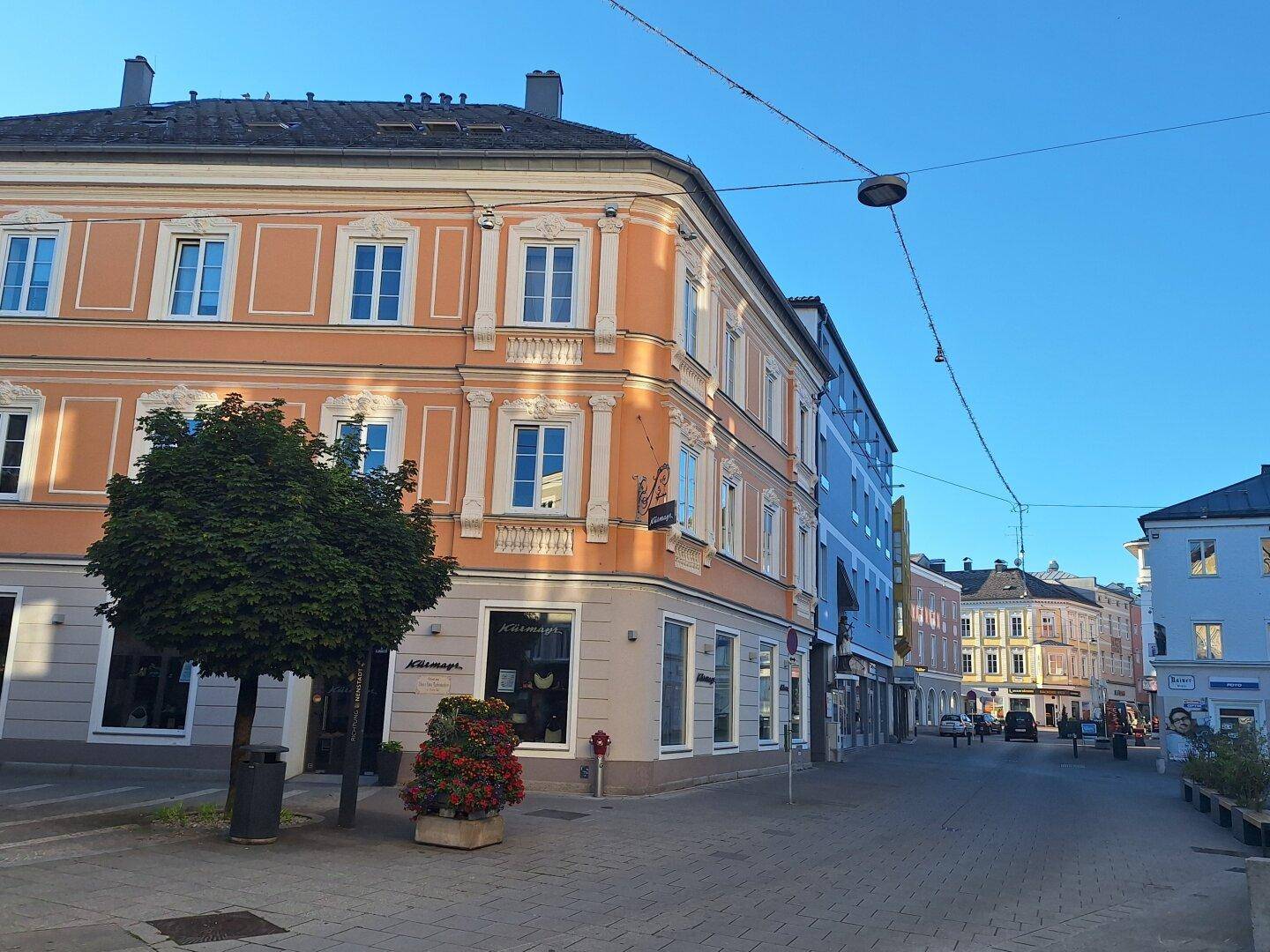 Blick auf eine belebte Straße mit historischen Gebäuden und Geschäften unter blauem Himmel am Morgen.
