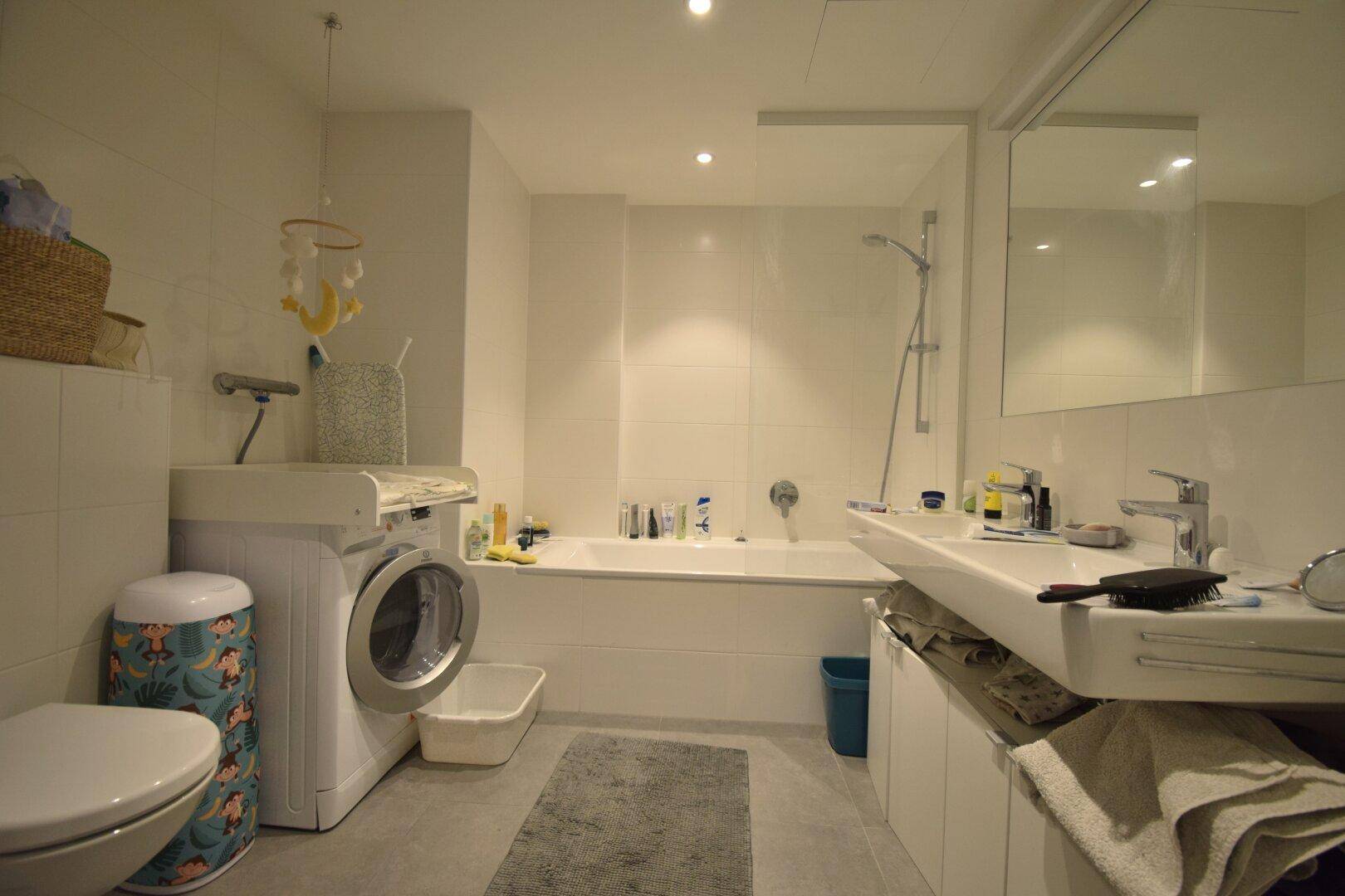 Modernes Badezimmer mit Badewanne, Dusche, WC, Waschmaschine und Wickeltisch.