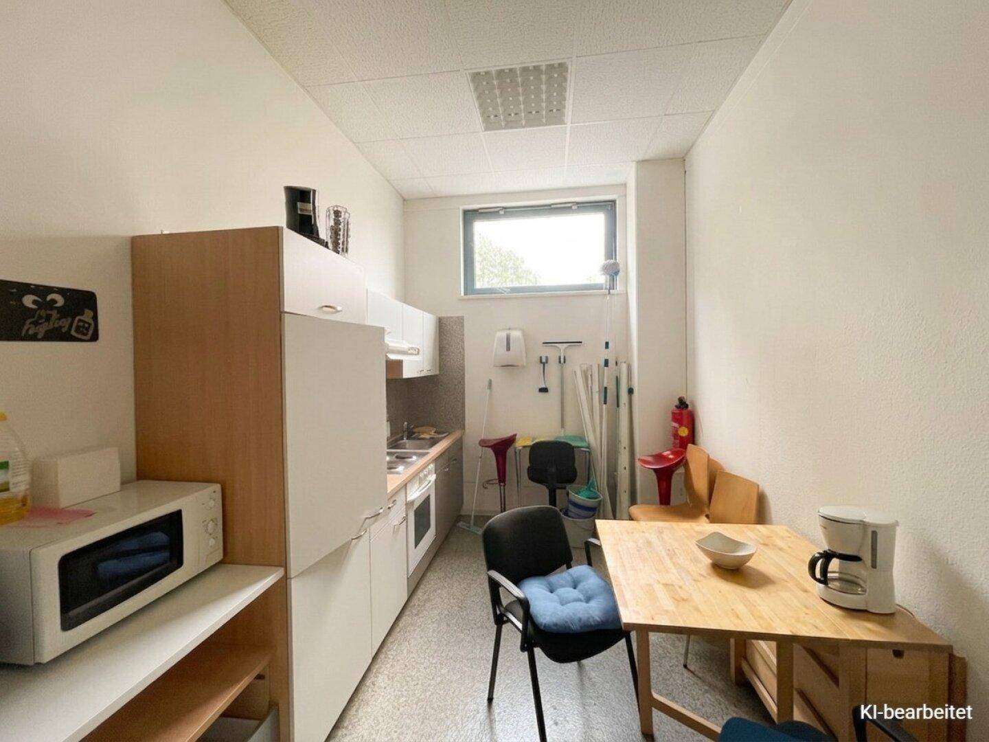 Kleine Küchenzeile oder Pausenraum mit einfachen Möbeln, Mikrowelle und einem Fenster für natürliche Belüftung.