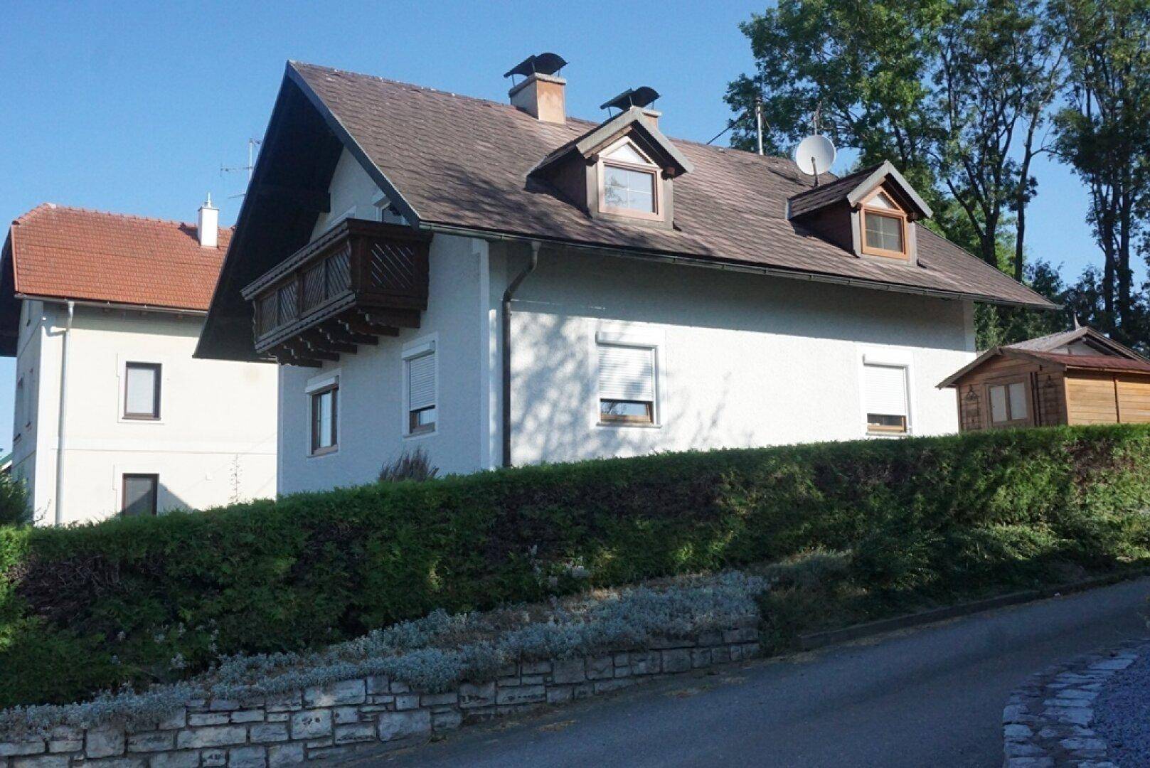 Seitenansicht des Hauses mit kleinem Holzbalkon und Rollläden an den Fenstern.