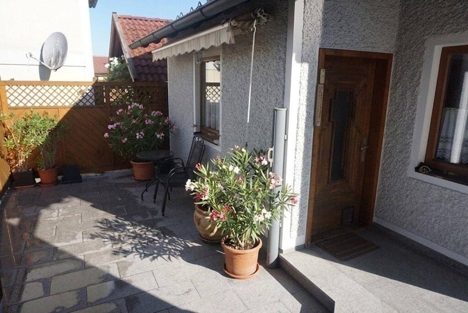 Sonnige Terrasse mit Sitzgelegenheiten und vielen Topfpflanzen, ideal zum Entspannen im Freien.