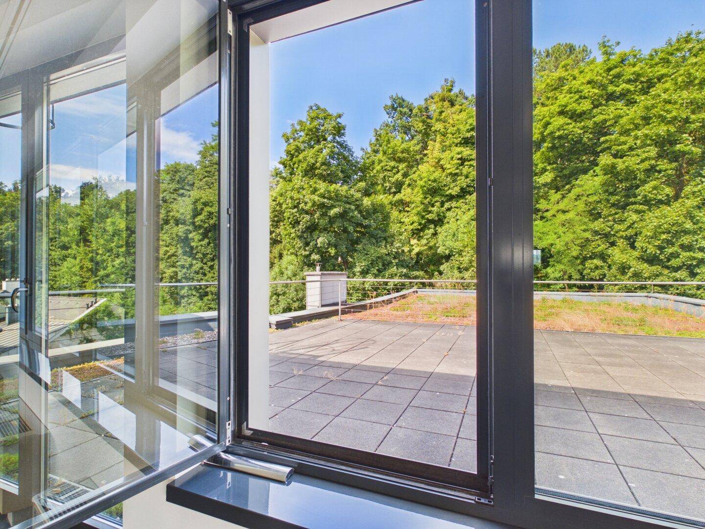 Große Dachterrasse mit Fliesenboden und weitem Blick auf grüne Bäume unter blauem Himmel.