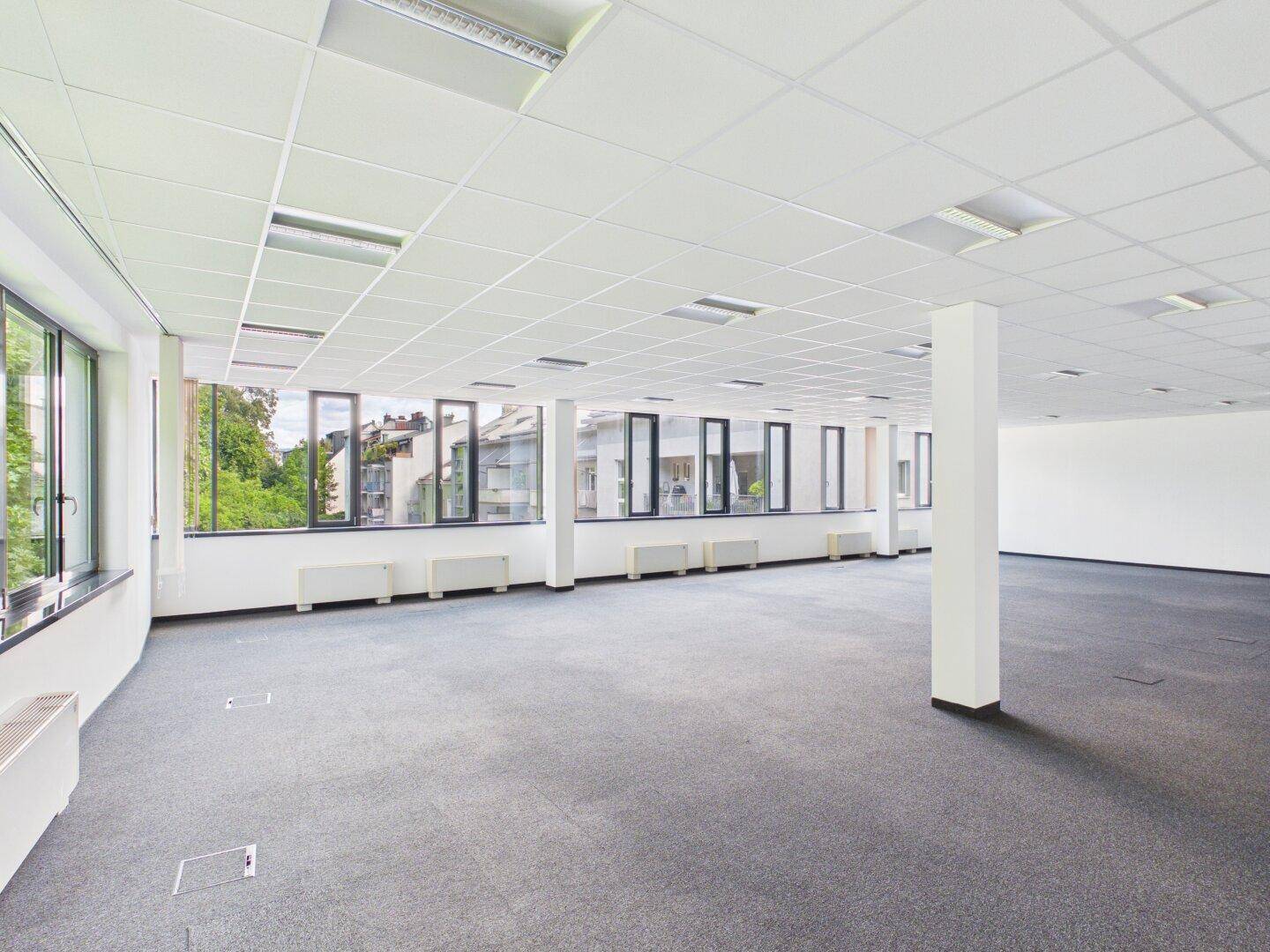 Weitläufiges Büro mit Teppichboden, Säulen und Fenstern mit Blick auf die Stadt.