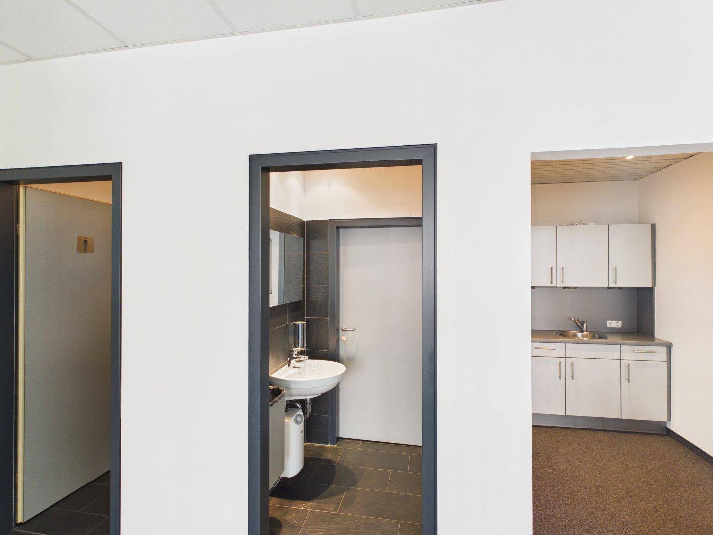 Modernes Badezimmer mit Waschbecken, Spiegel und dunklen Fliesen im Bürogebäude.