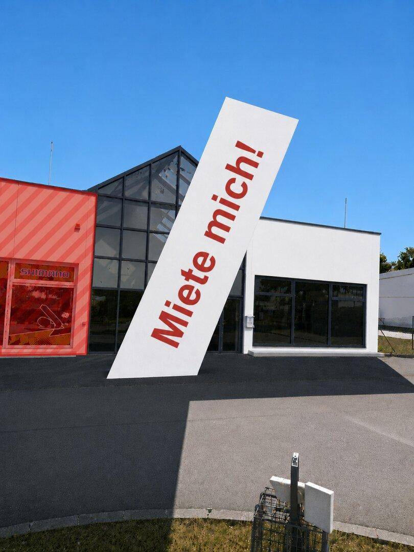 Außenansicht eines modernen Geschäftsgebäudes mit einer markanten Glasfassade und einem großen "Miete mich!" Schild.