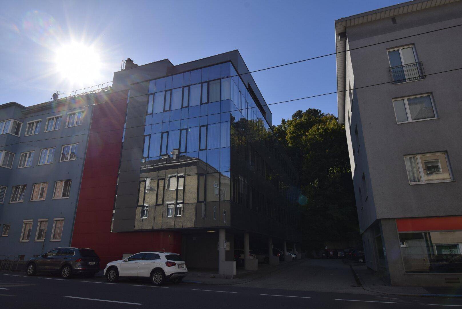 Modernes Bürogebäude mit Glasfassade und Tiefgaragenzufahrt unter strahlendem Sonnenschein.