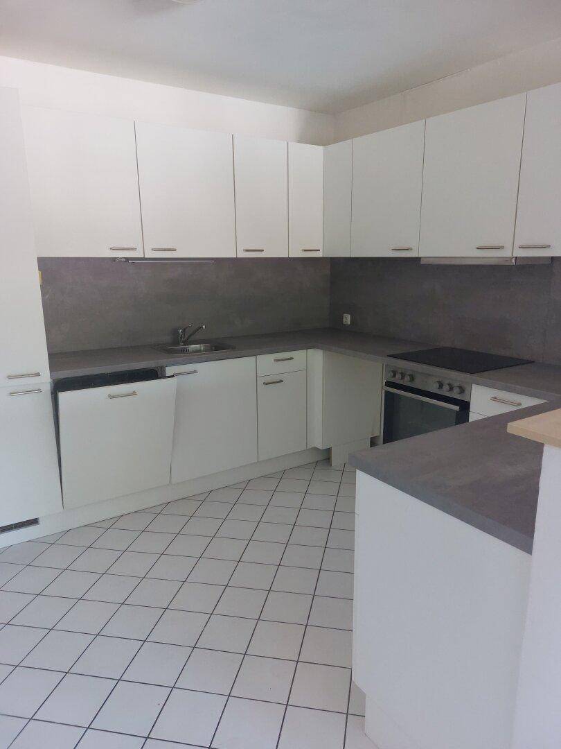 Moderne Einbauküche mit weißen Schränken, grauen Arbeitsplatten und Fliesenboden, ausgestattet mit Backofen und Kochfeld.