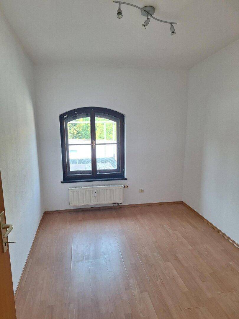 Freundliches Zimmer mit Laminatboden und einem Bogenfenster, das für eine angenehme Helligkeit sorgt.