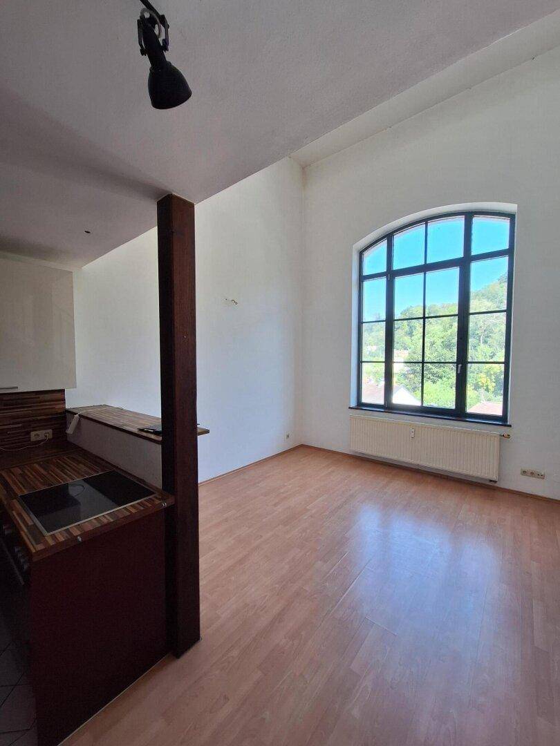 Heller Raum mit Laminatboden und einem großen Bogenfenster, das viel Tageslicht hereinlässt.