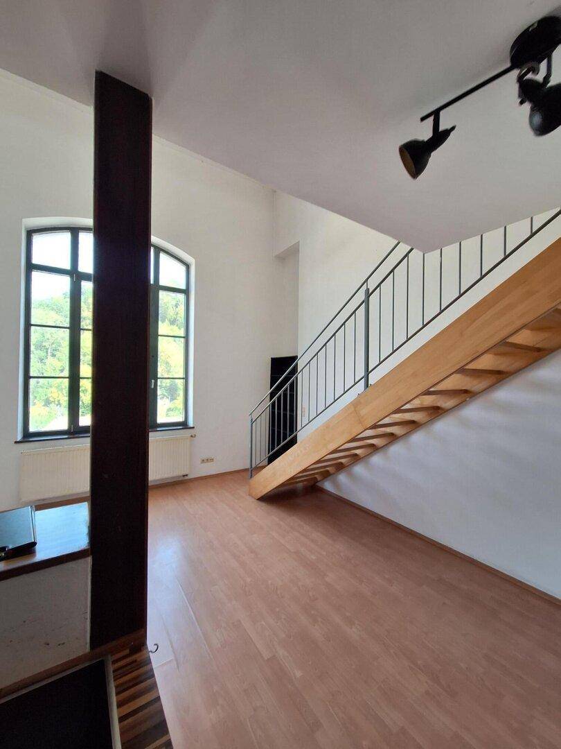 Heller Wohnbereich mit Holztreppe, Laminatboden und großen Fenstern mit Blick ins Grüne.
