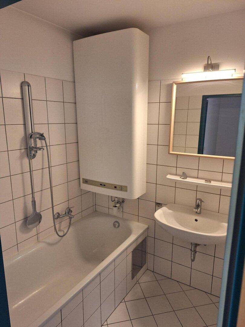 Gefliestes Badezimmer mit Badewanne, Duschvorrichtung, Waschbecken und Wandspiegel.
