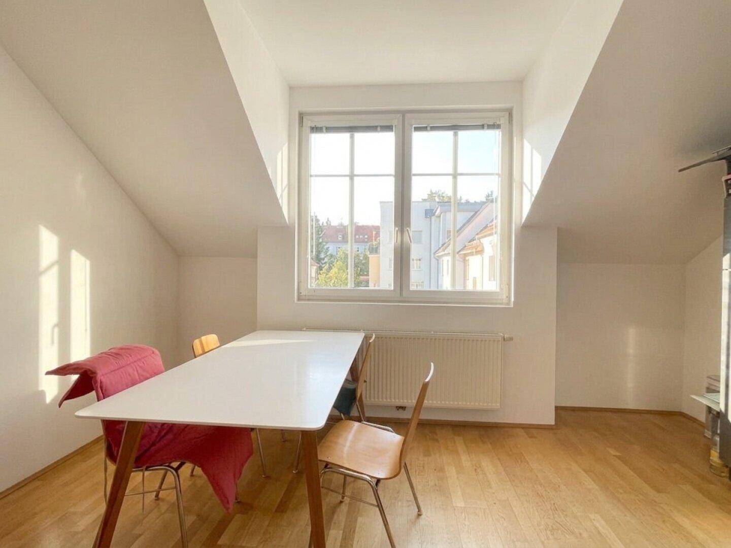 Heller Essbereich im Dachgeschoss mit großem Fenster, Holzboden und schrägen Wänden.
