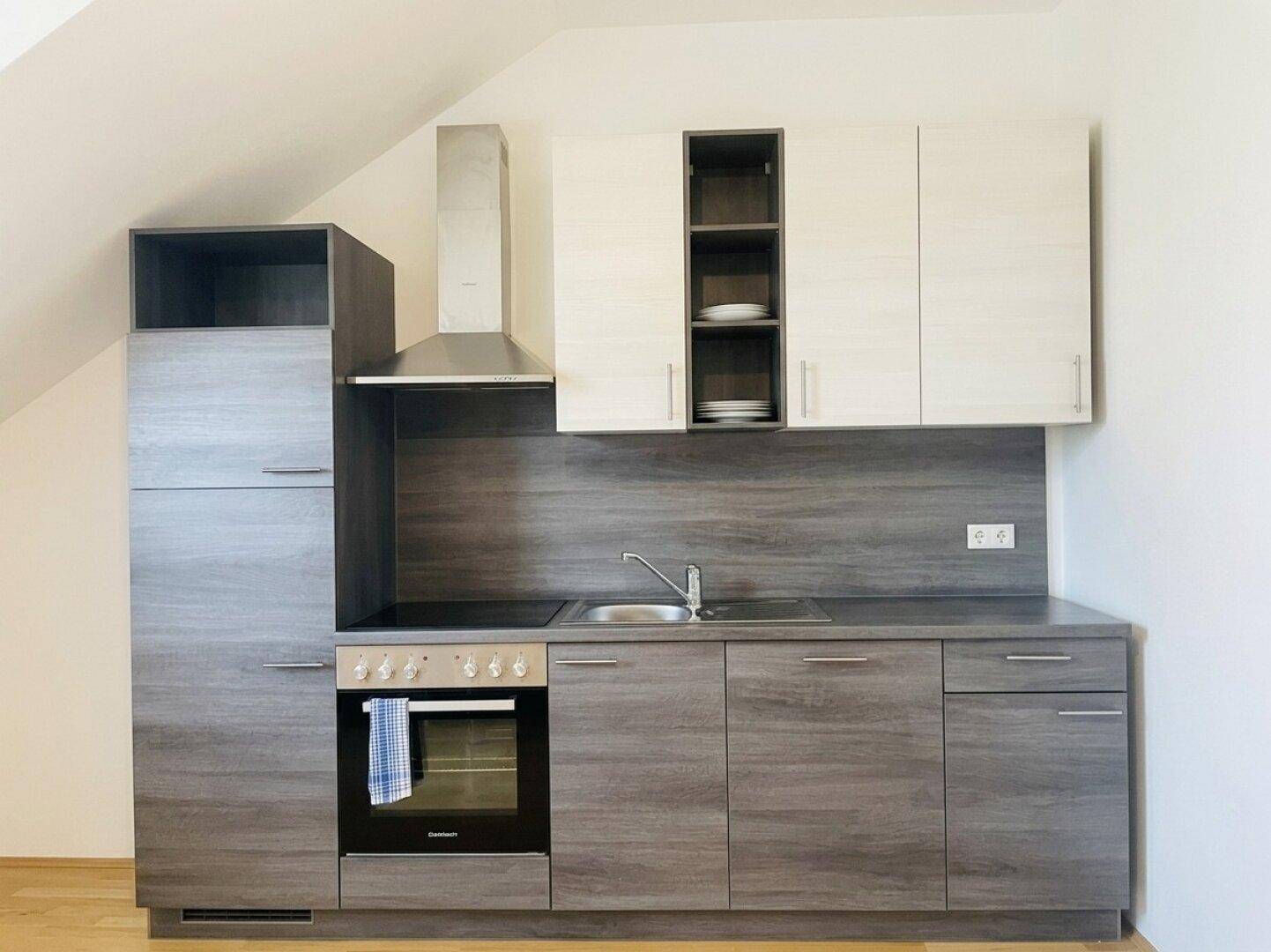 Kompakte Einbauküche mit modernen Holzfronten, integriertem Backofen und Dunstabzugshaube im Dachgeschoss.