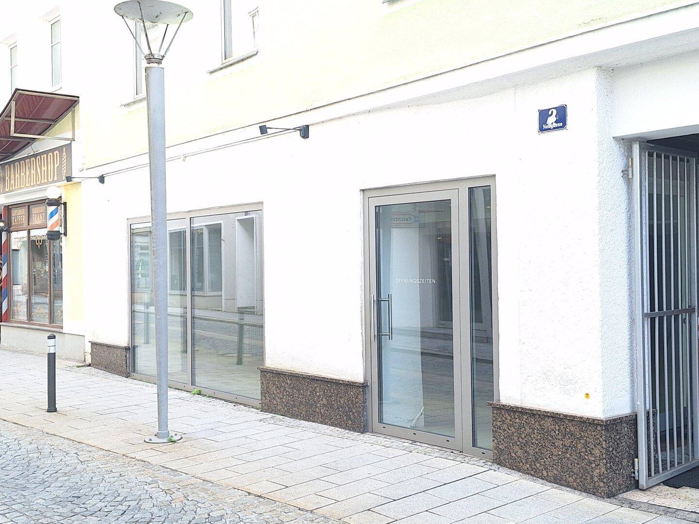 Außenansicht eines Geschäftsgebäudes mit großen Glasfronten und Eingangstür an einer Straße.
