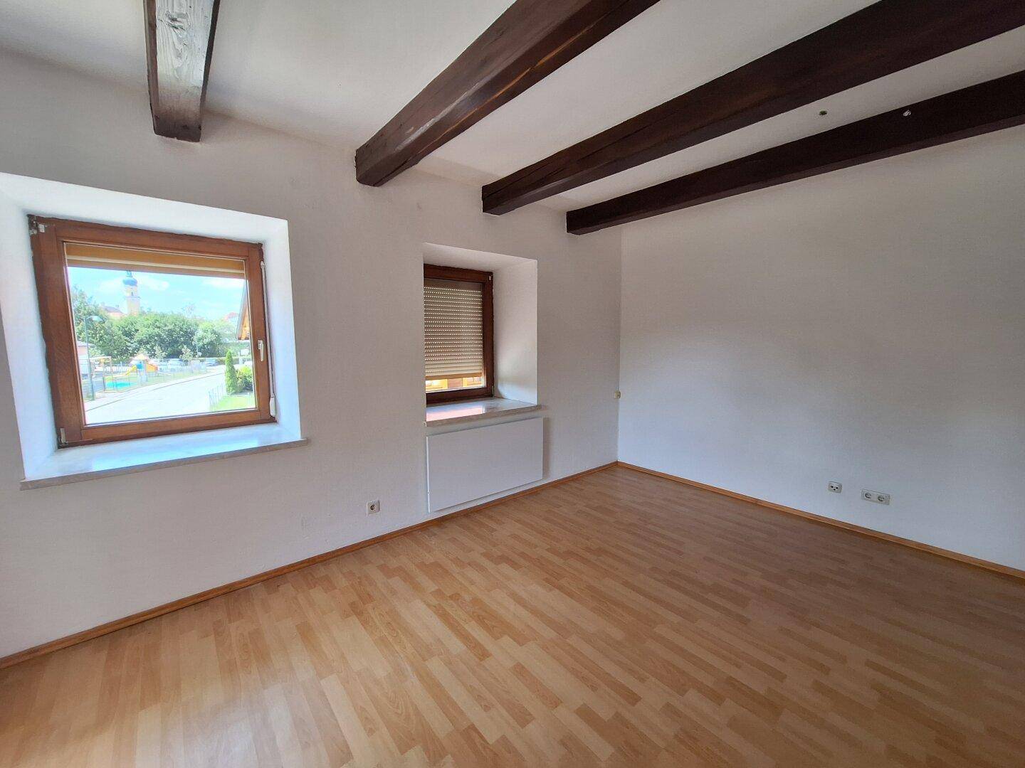 Helles Zimmer mit Holzbalken an der Decke und Parkettboden.