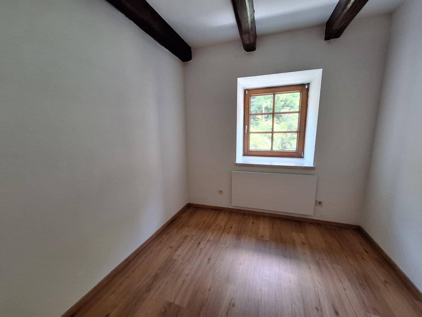 Gemütliches Schlafzimmer mit Holzbalken, Parkettboden und einem Fenster.