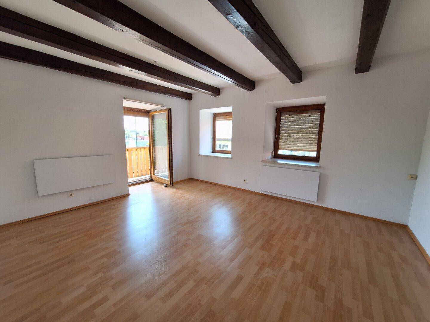 Geräumiges Zimmer mit Holzbalken, Parkettboden und Zugang zum Balkon.