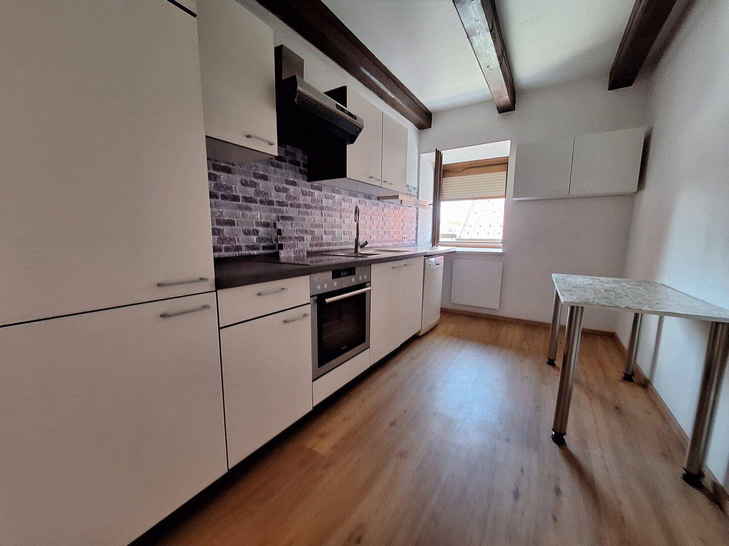 Moderne Küche mit weißen Schränken, dunkler Arbeitsplatte und Holzbalken.