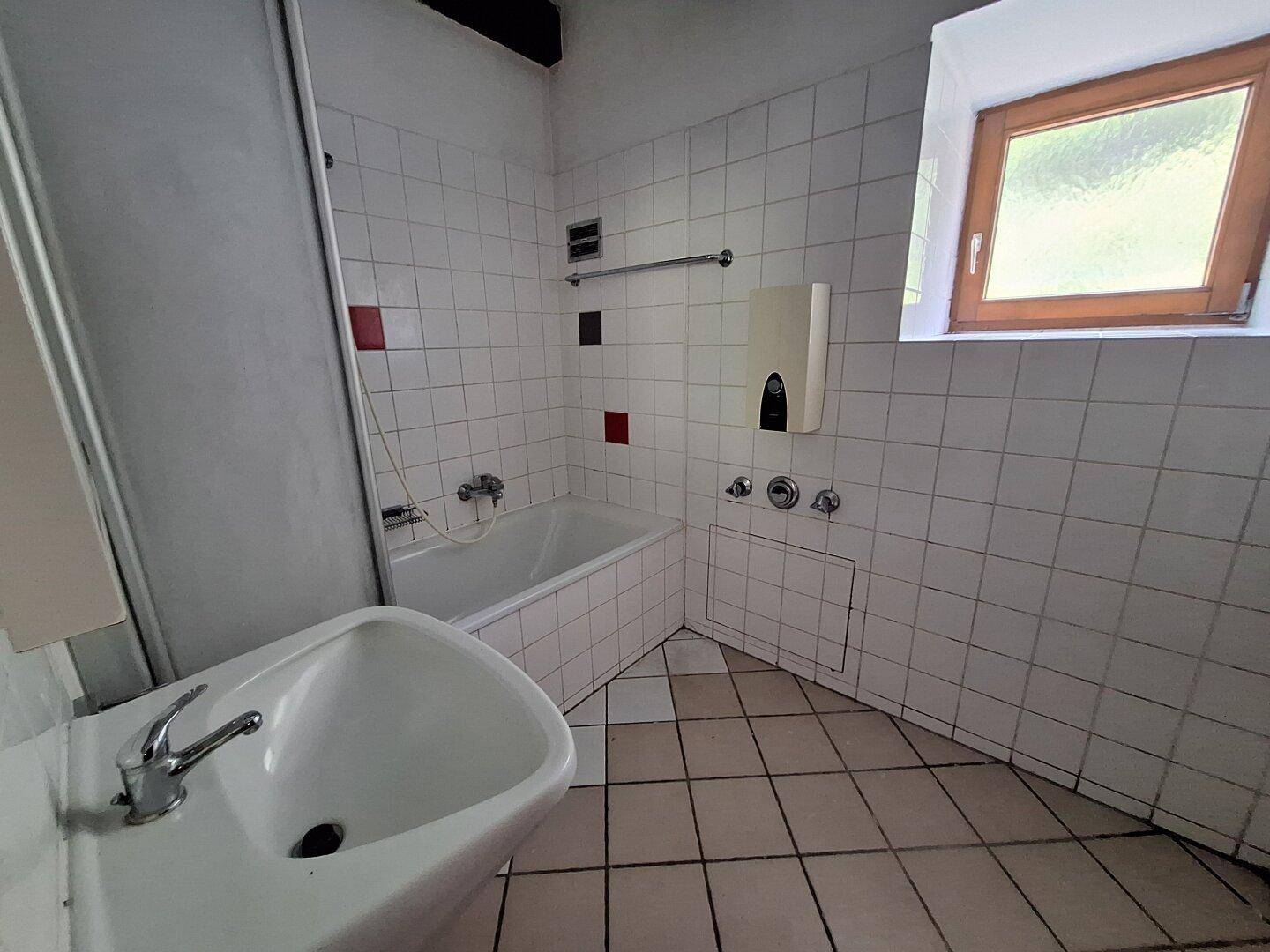 Gefliestes Badezimmer mit Badewanne, Dusche, Waschbecken und Fenster.