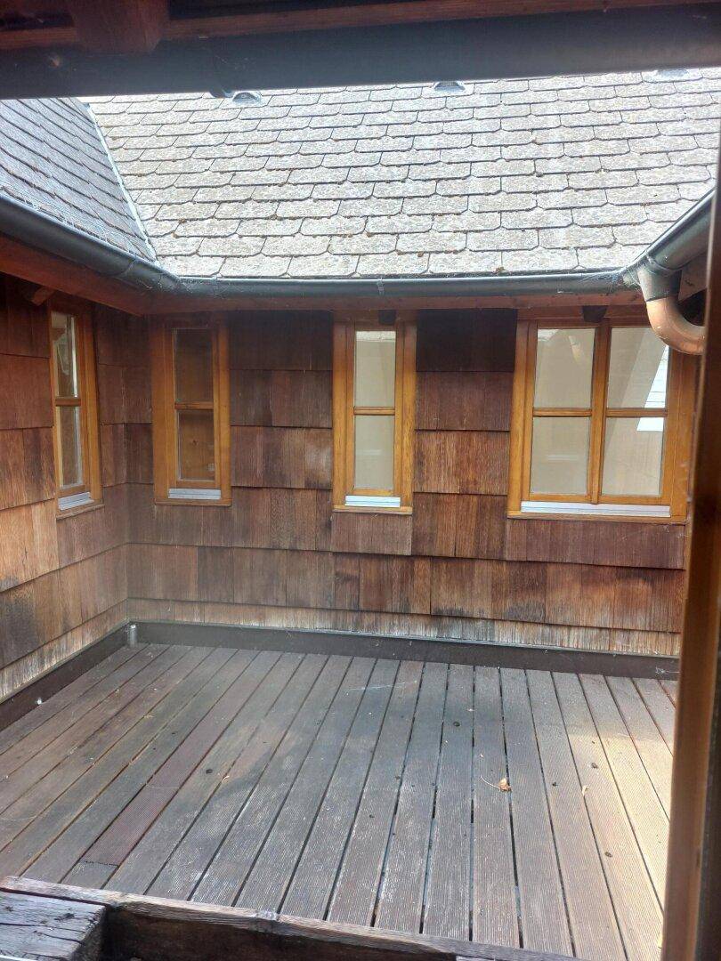 Kleine, geschützte Terrasse mit Holzdeck und Holzschindelfassade unter einem Ziegeldach.
