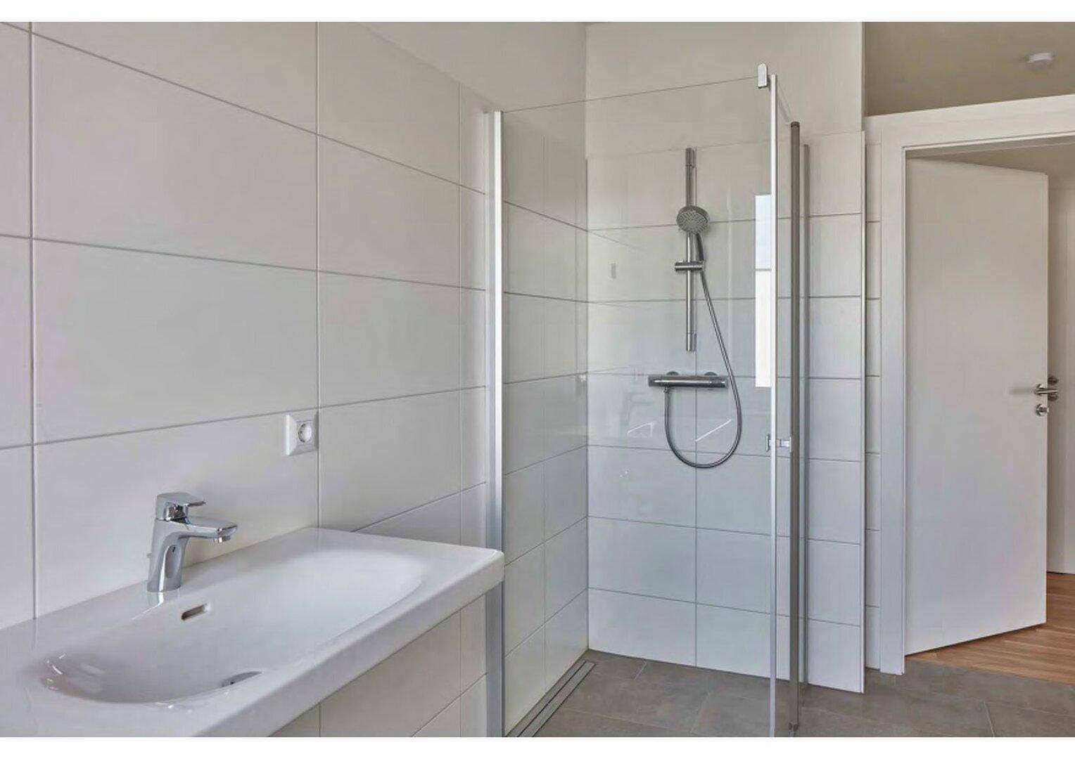 Helles, modernes Badezimmer mit ebenerdiger Dusche, Einzelwaschbecken und weißen Fliesen.