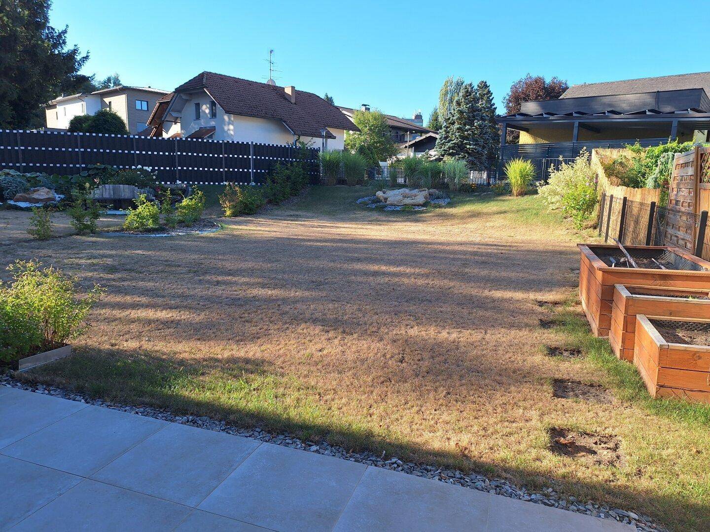 Großer Gartenbereich mit Rasenfläche, Hochbeeten und umzäuntem Grundstück in sonniger Lage.