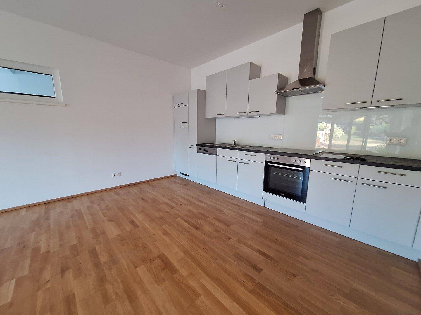 Moderne Einbauküche mit hellgrauen Schränken, dunkler Arbeitsplatte und Holzboden.