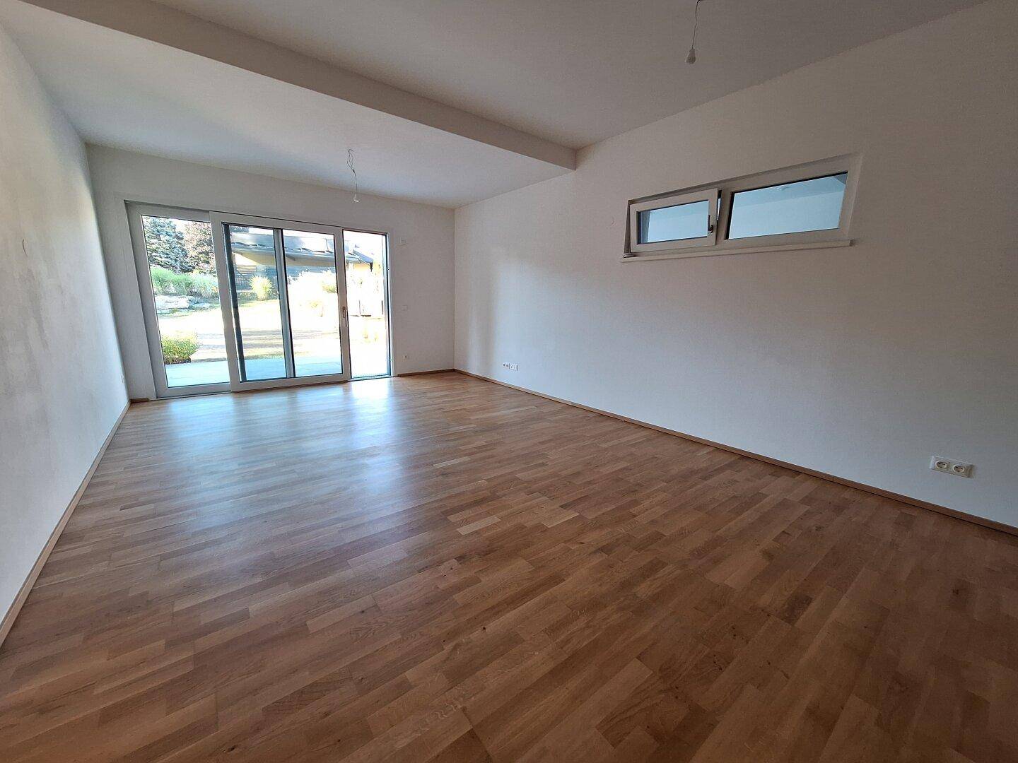 Heller, leerer Wohnraum mit großen Schiebetüren und Holzboden, bietet Zugang zum Außenbereich.