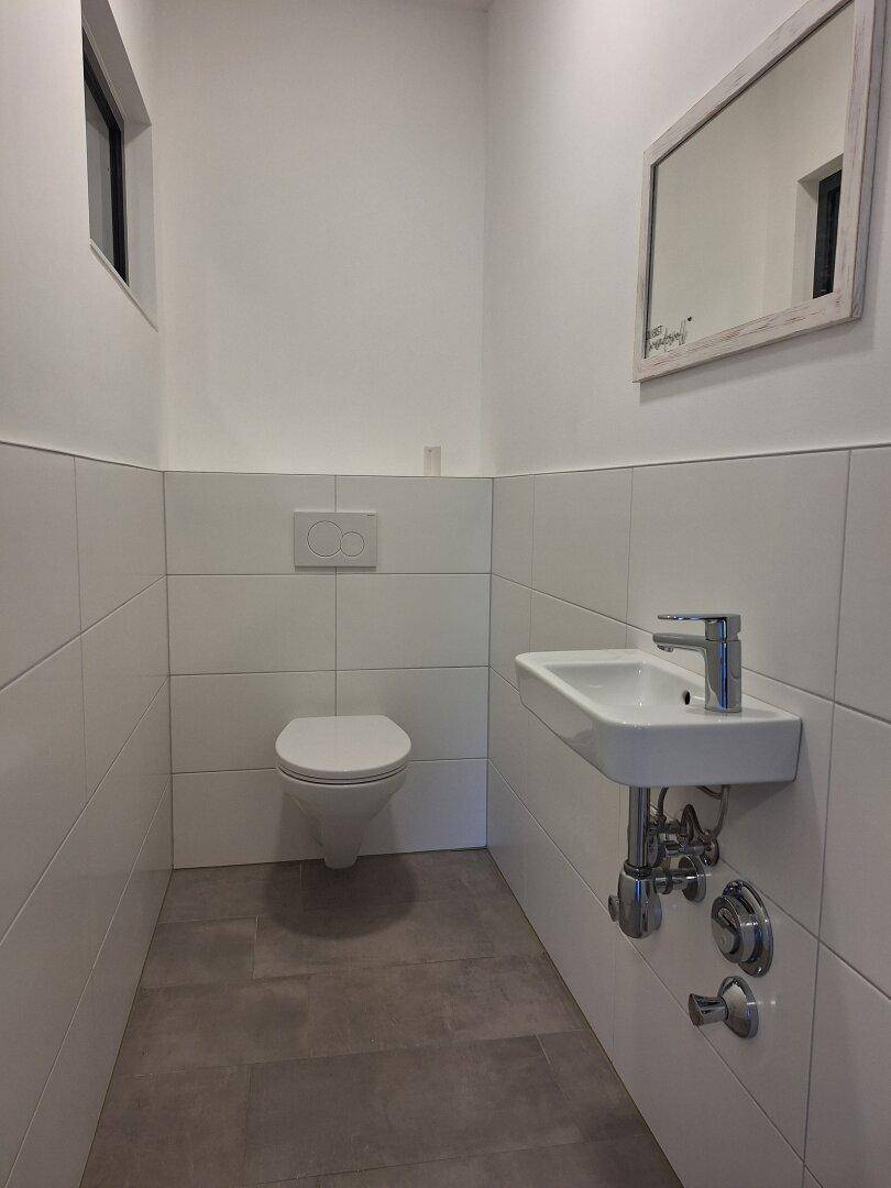 Modernes Gäste-WC mit wandhängendem WC, kleinem Waschbecken und Fenster.