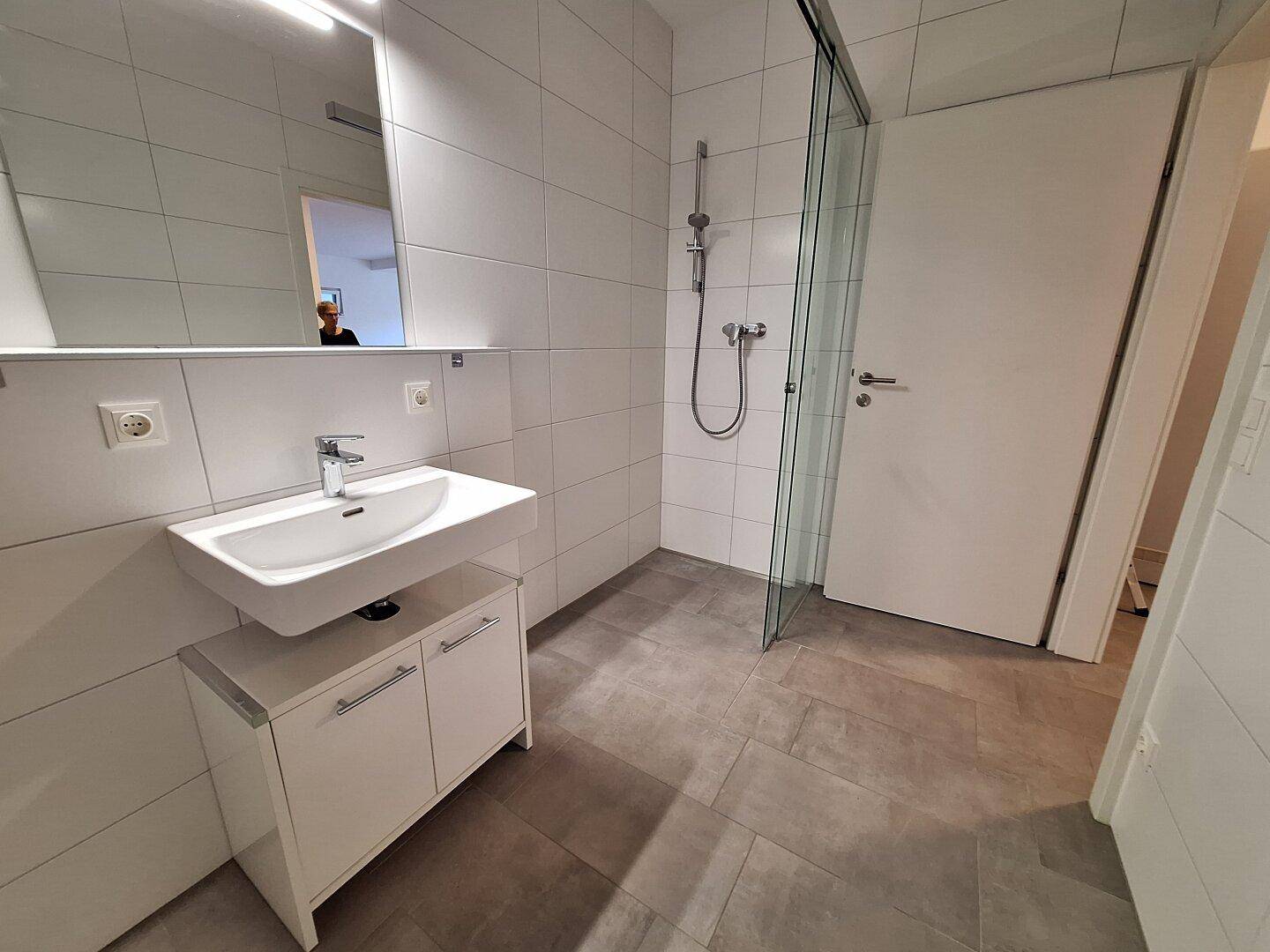 Helles Badezimmer mit modernem Waschbecken, Spiegelschrank und ebenerdiger Dusche.