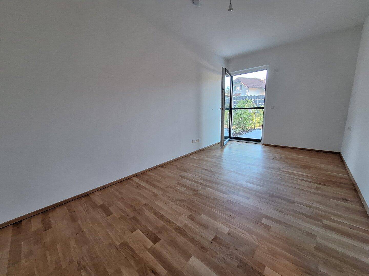 Heller Raum mit Holzboden und Zugang zu einem Außenbereich, ideal als Schlafzimmer.