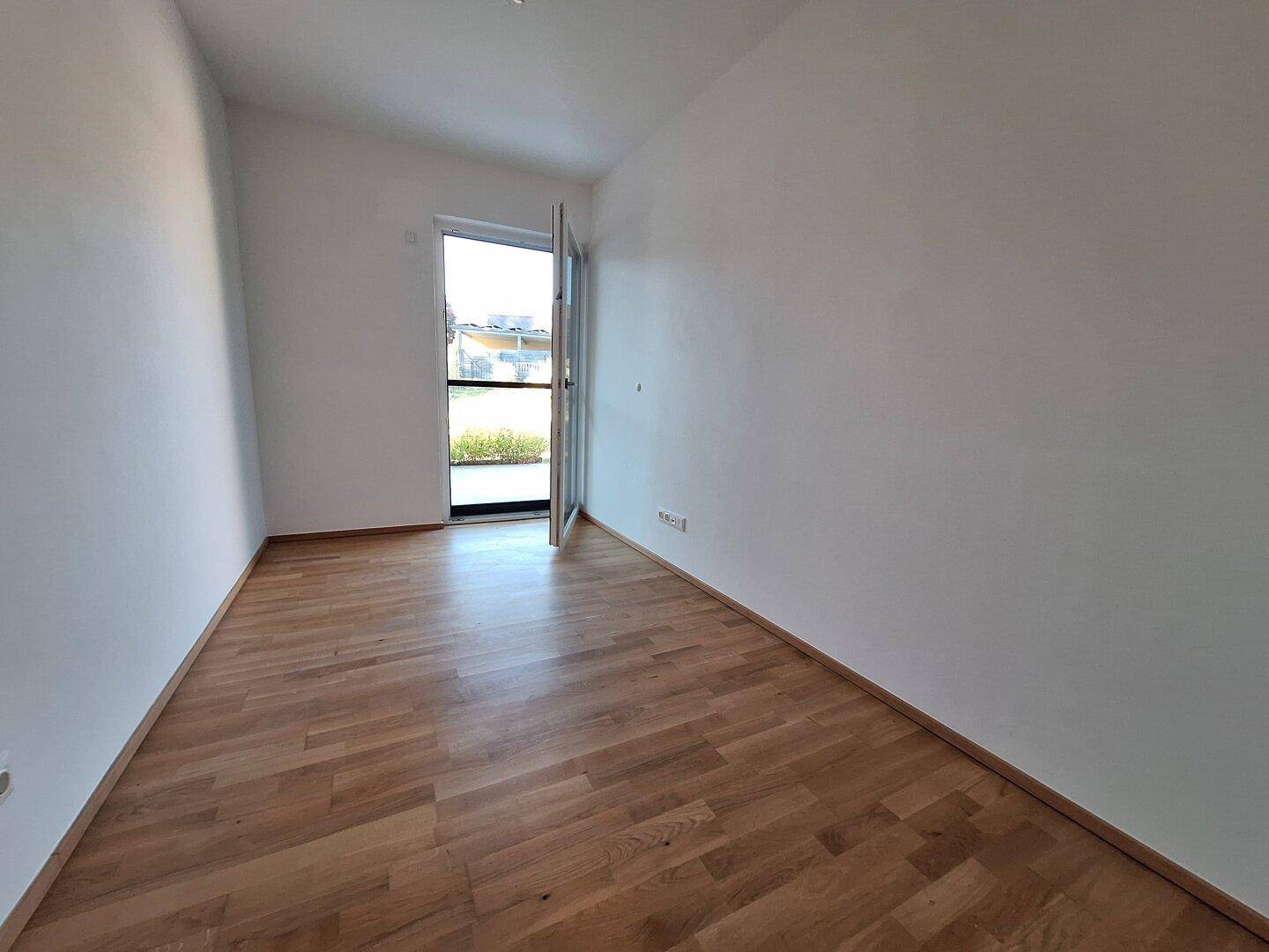Leerer Raum mit Holzboden und Tür zum Garten, bietet viel Tageslicht.