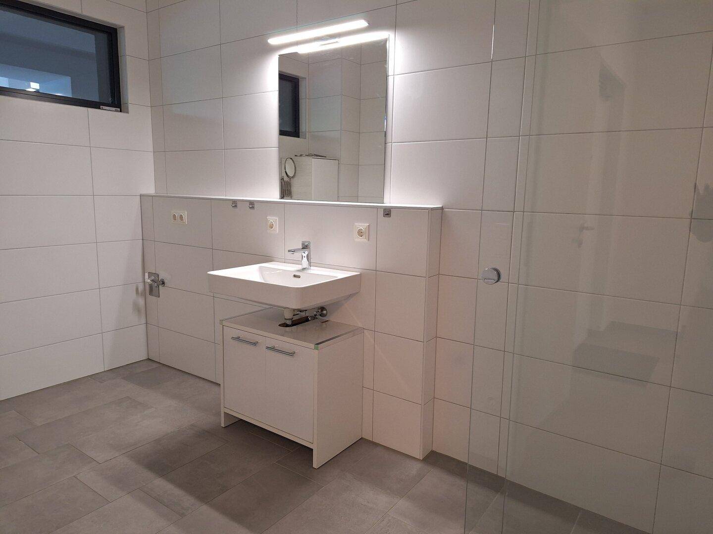 Modernes Badezimmer mit großem Spiegel, Waschbecken und weißen Fliesen.