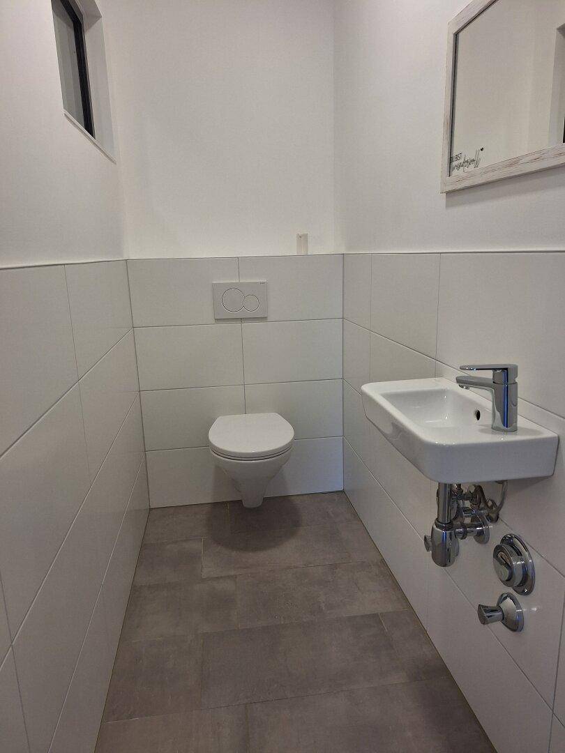 Modernes Gäste-WC mit wandhängendem WC, kleinem Waschbecken und Fenster.