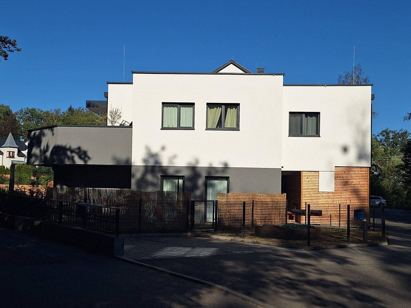 Moderne Wohnhausfassade mit weißem und grauem Putz sowie Holzelementen.