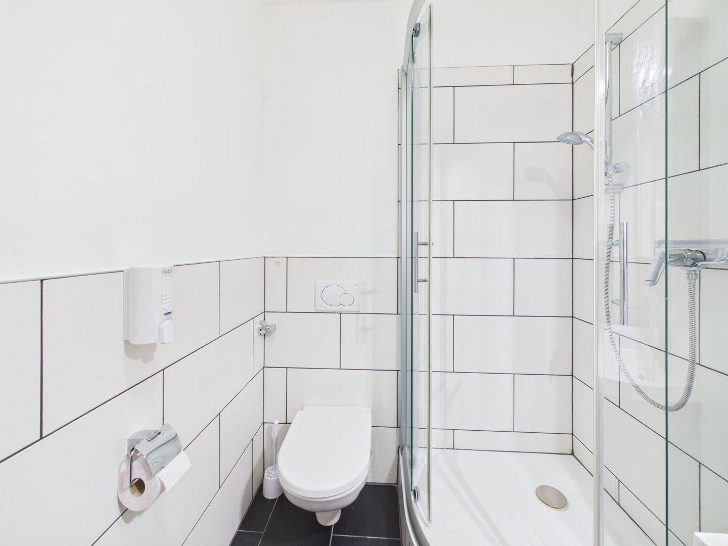 Modernes Badezimmer mit weiß gefliesten Wänden, Dusche und wandhängendem WC.