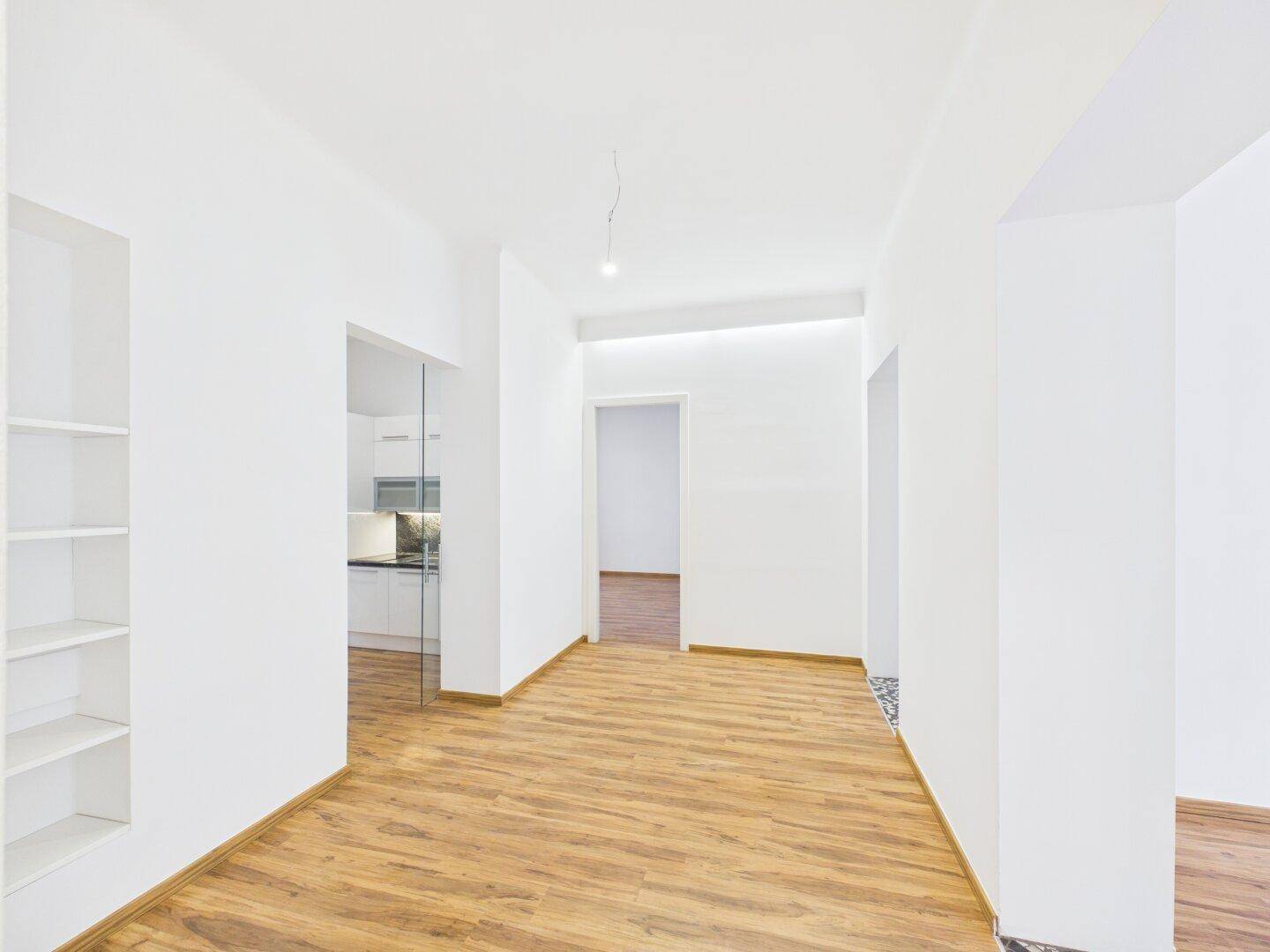 Heller Flur mit Laminatboden, Einbauregal und Blick in die moderne Küche.