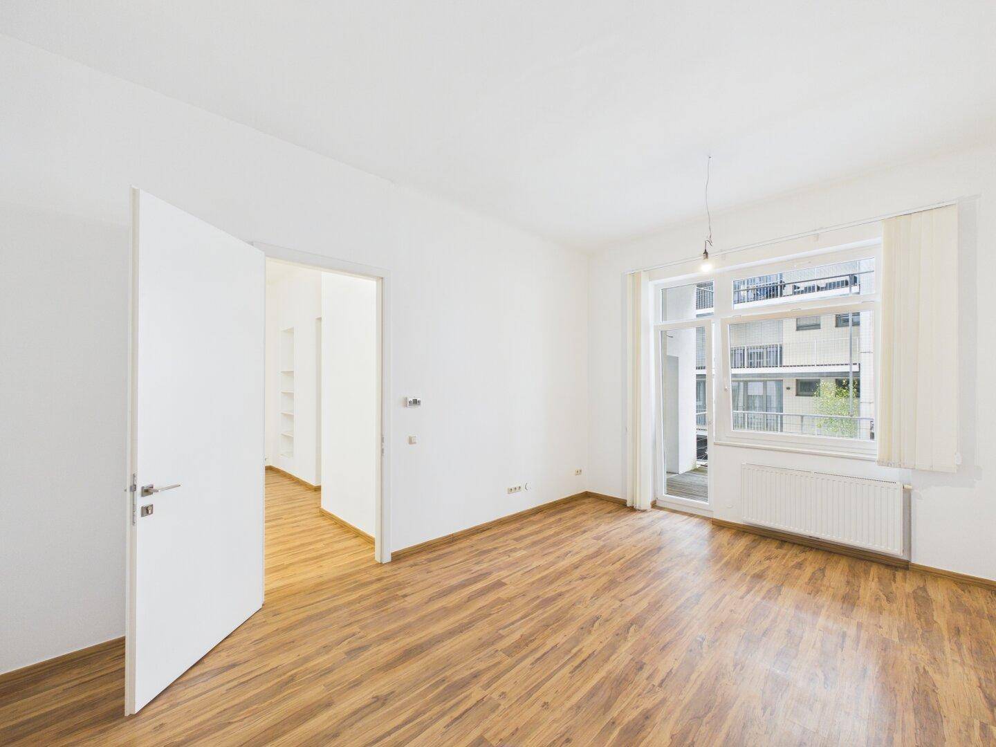Helles Zimmer mit Laminatboden und direktem Zugang zu einem Balkon.