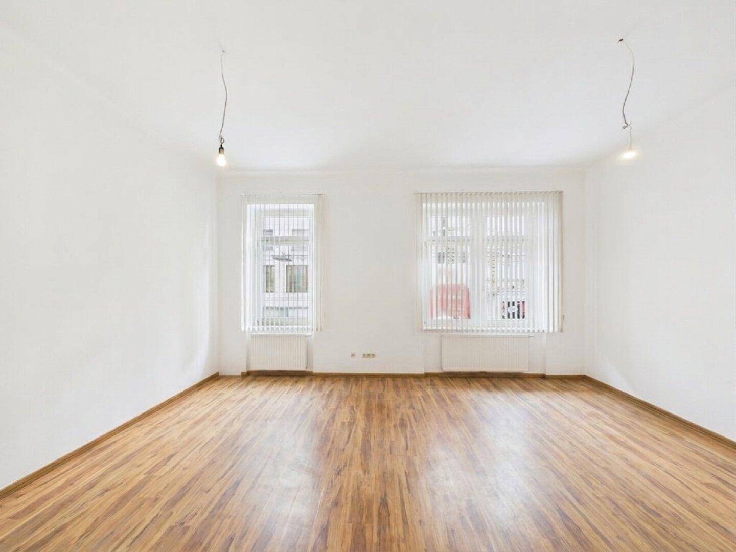 Geräumiges, helles Zimmer mit Laminatboden und zwei großen Fenstern.