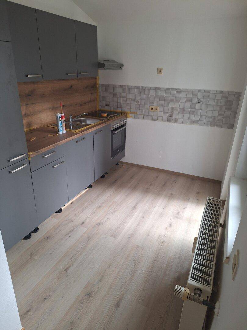 Funktionale Küche mit grauen Unterschränken, Holzdekor und einem Heizkörper unter dem Fenster.